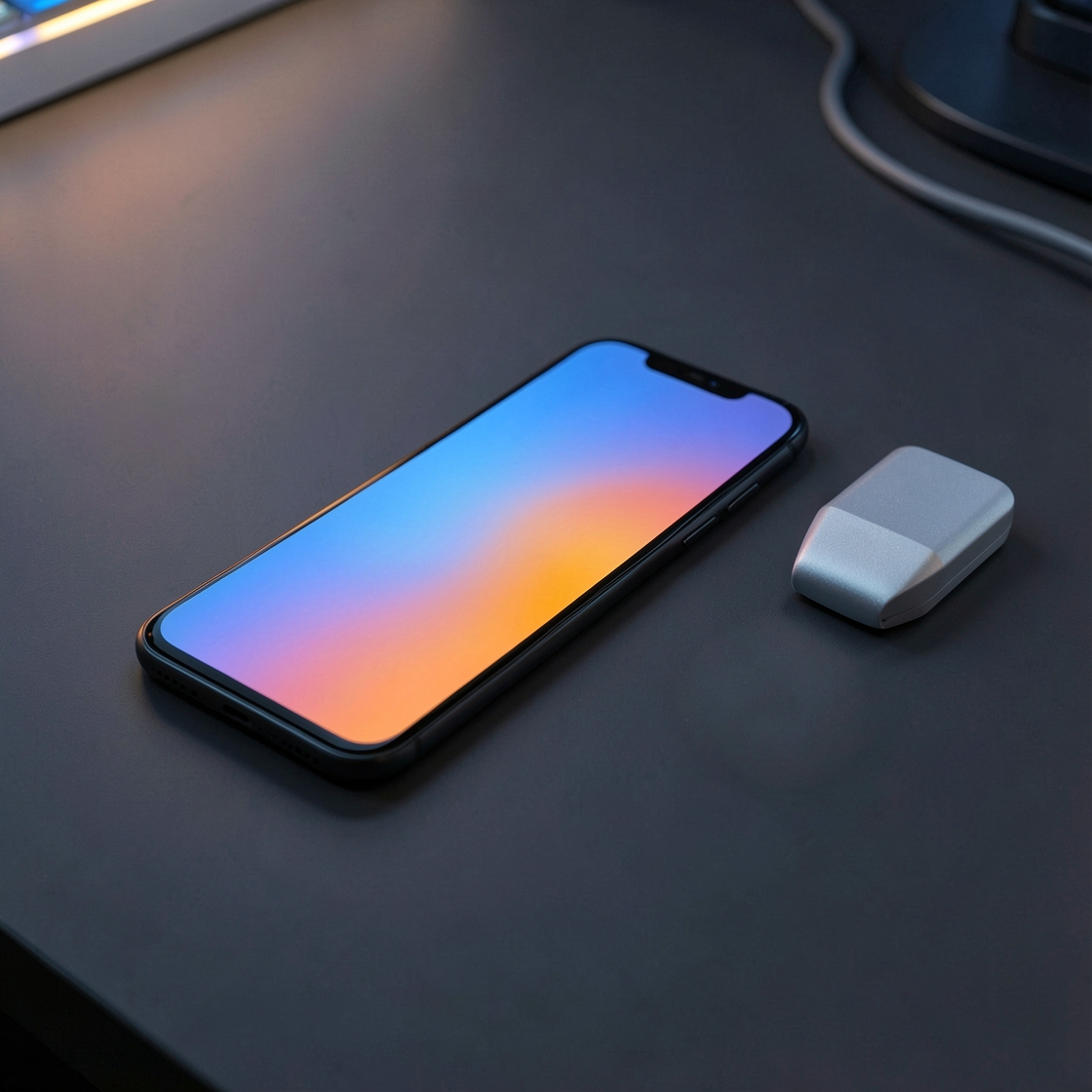 A generic smartphone with a blue and orange gradient screen beside a silver block on a dark desk