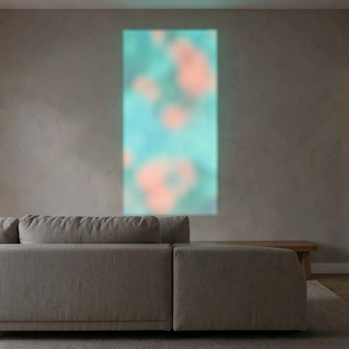 Teal and coral abstract light projected vertically on a bare wall above a linen sofa and low wooden shelf.