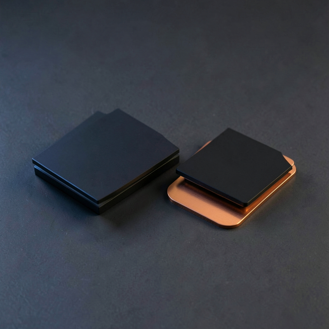 Two blank black chip-like packages, one resting on a copper plate, on a dark surface
