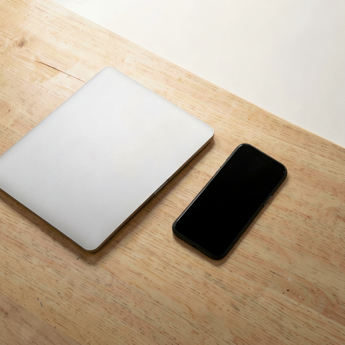 Conceptual illustration of a closed silver laptop beside a black phone on a wooden desk