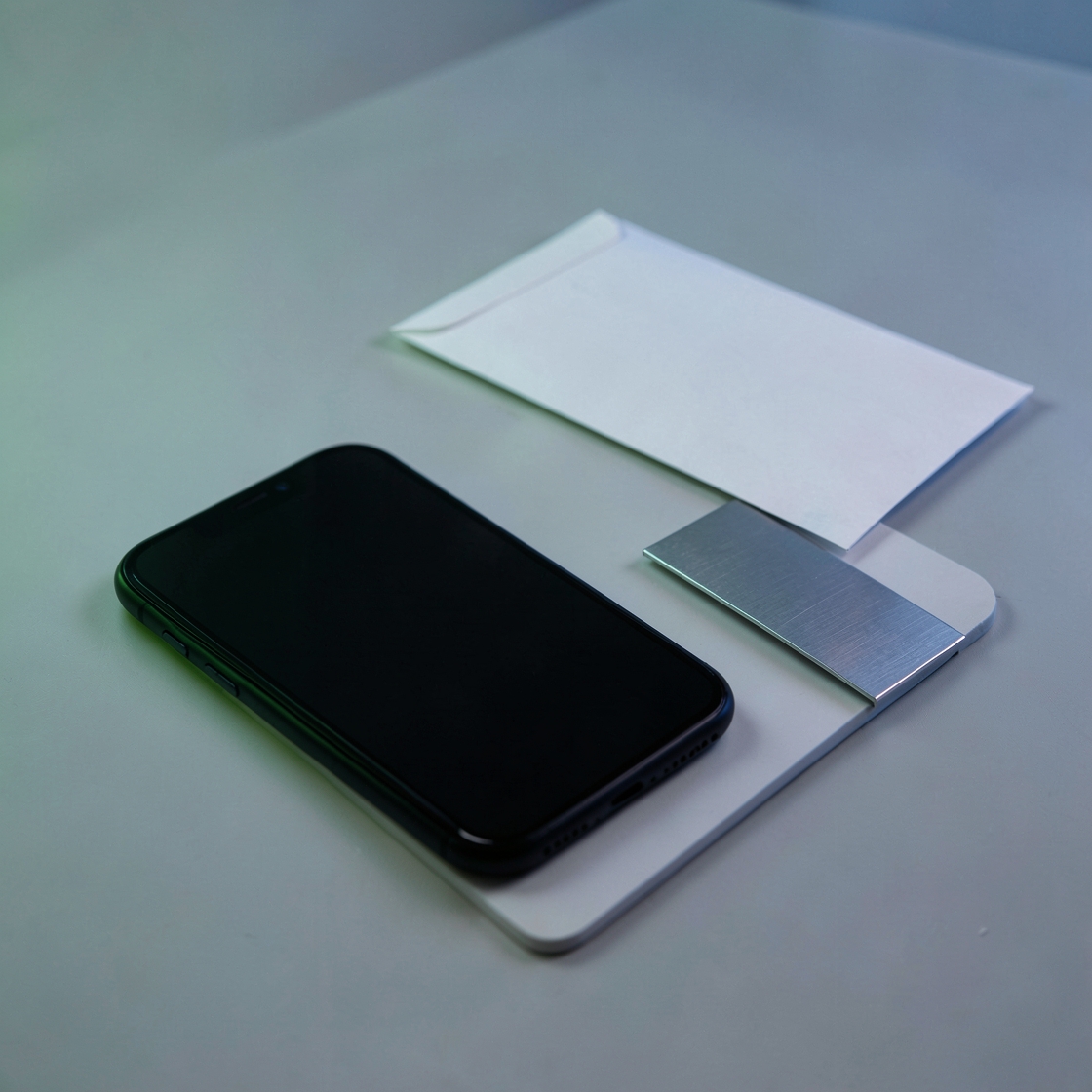 A dark-screen phone beside a blank envelope and a plain metal cover