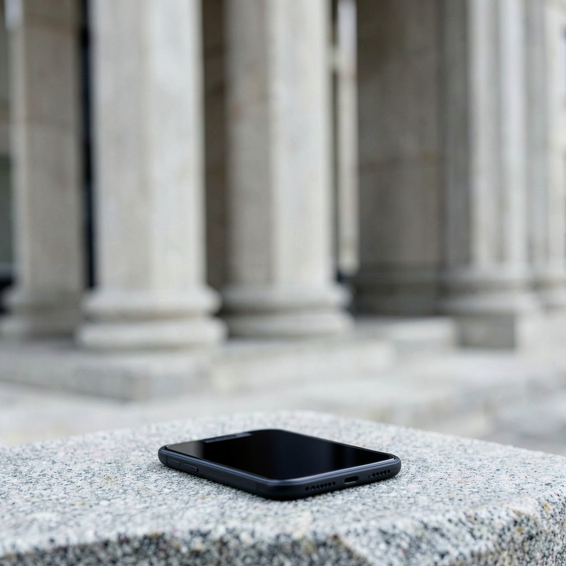 A blank-screen smartphone on a stone ledge with plain classical columns out of focus behind it.