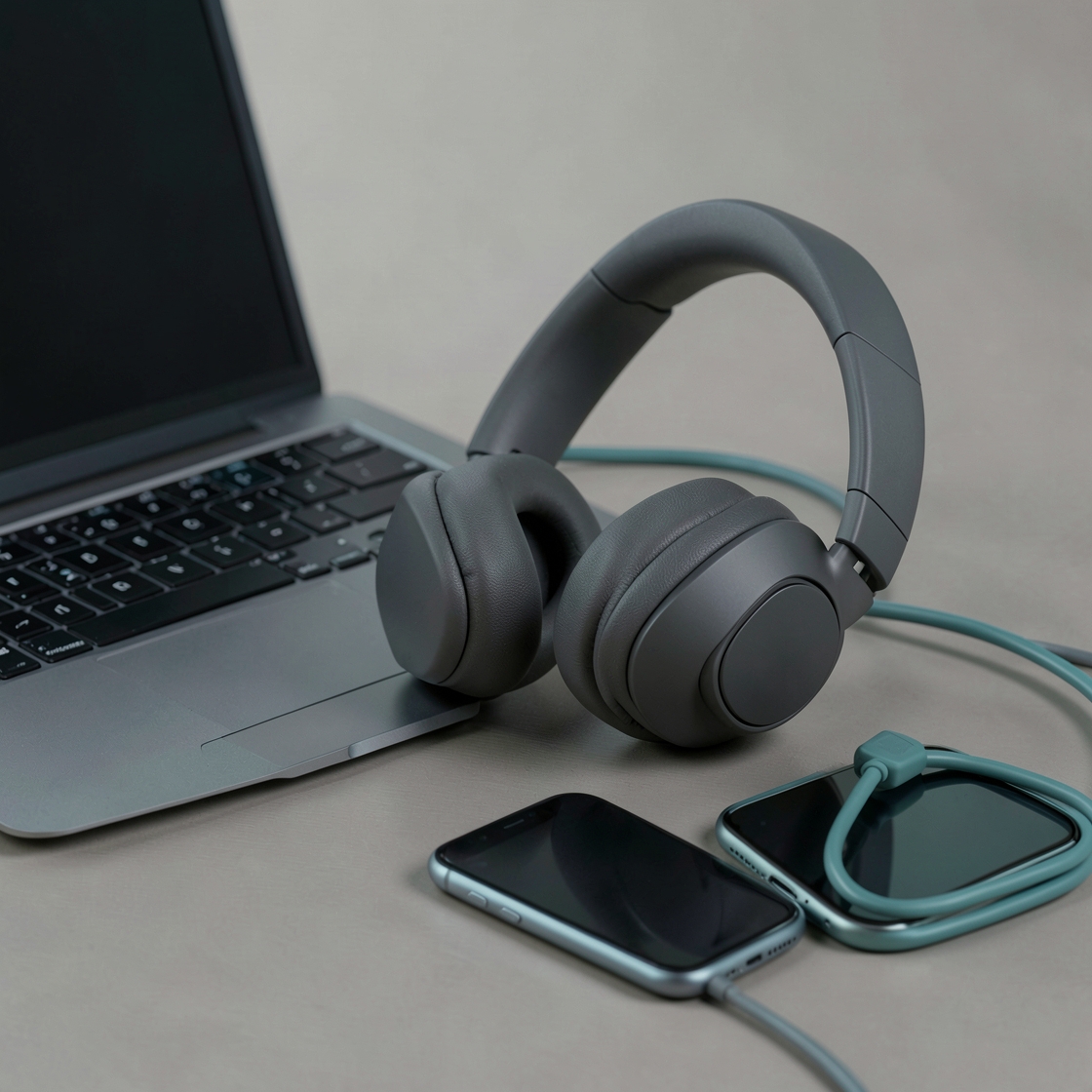 Generic over-ear headphones beside an open laptop, two smartphones and a teal USB cable.
