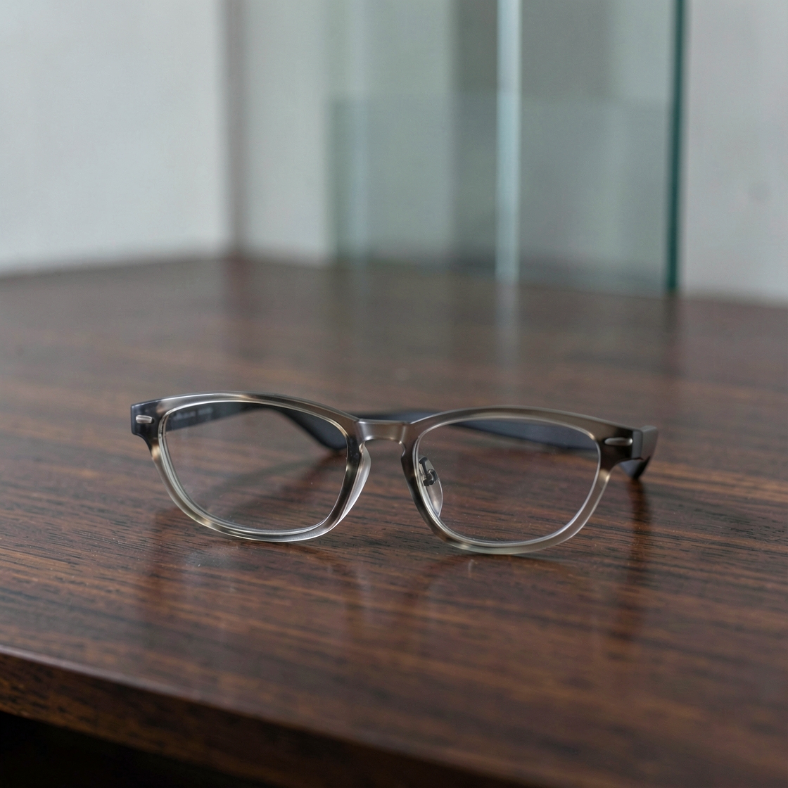 Conceptual unbranded gray eyeglasses resting on a wooden desk with a glass wall behind