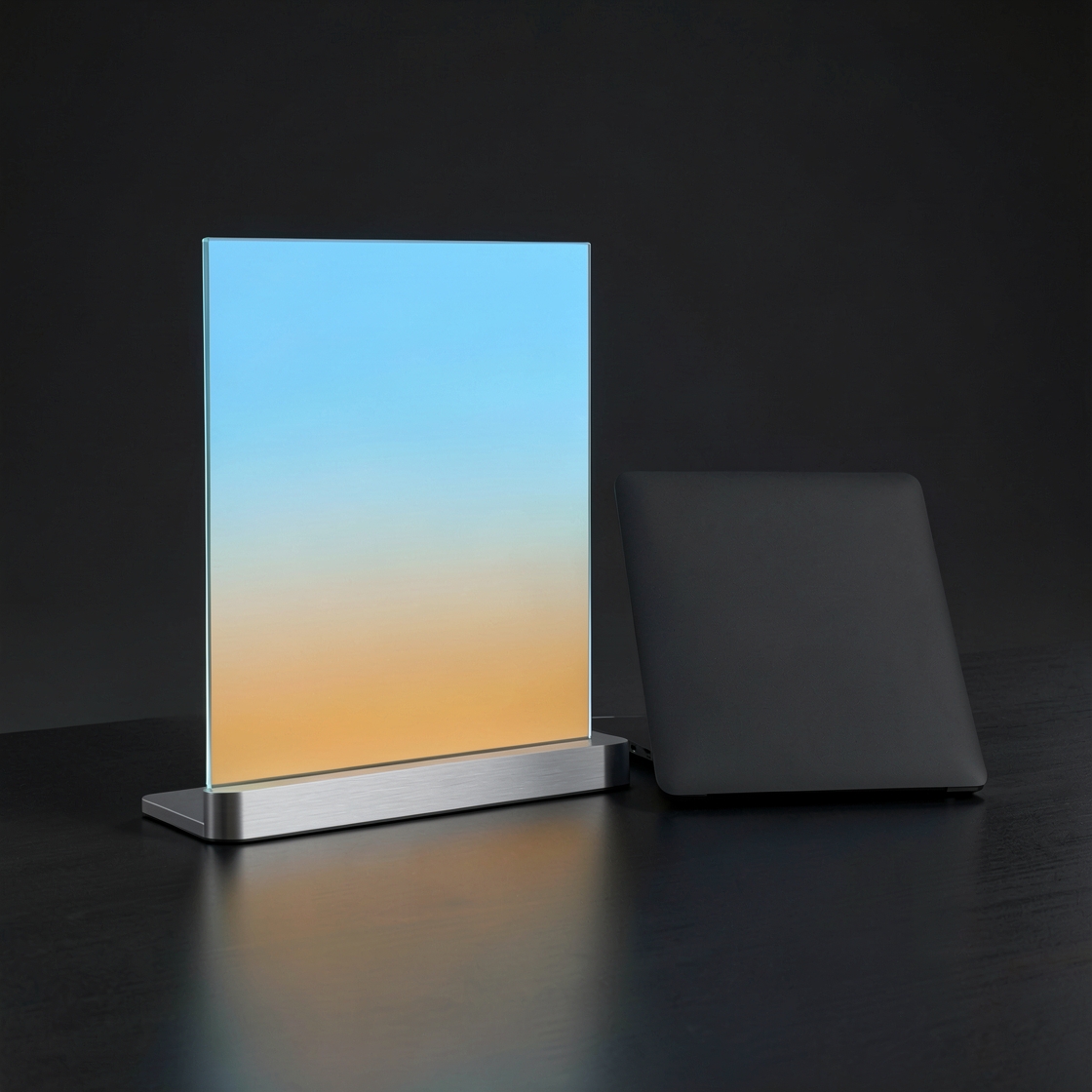 A glowing blue and amber glass panel beside a closed dark laptop on a studio desk.