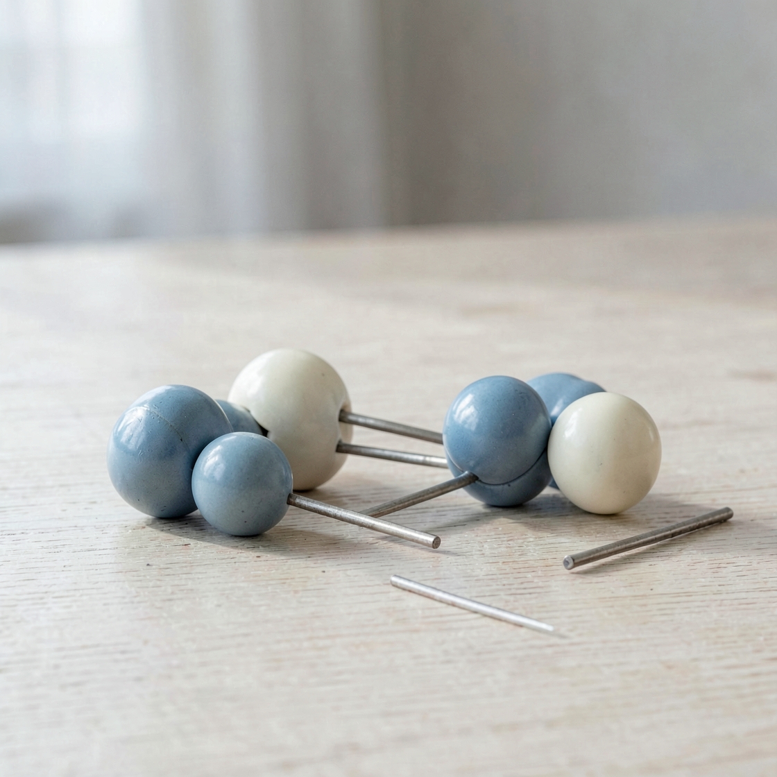 Blue and ivory ceramic spheres linked by metal rods, with loose rods on a pale table