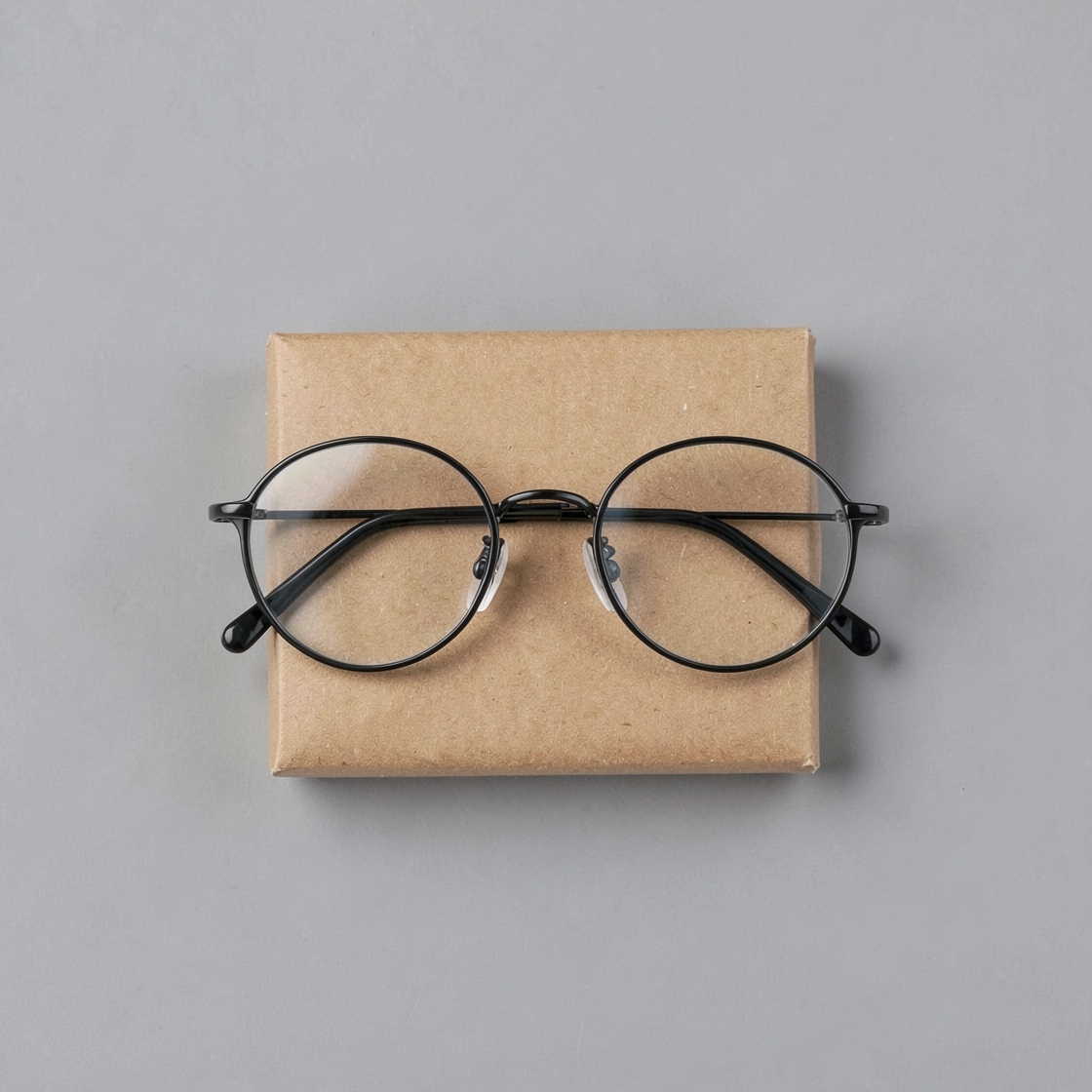 Generic round clear-lens glasses folded on a plain cardboard parcel