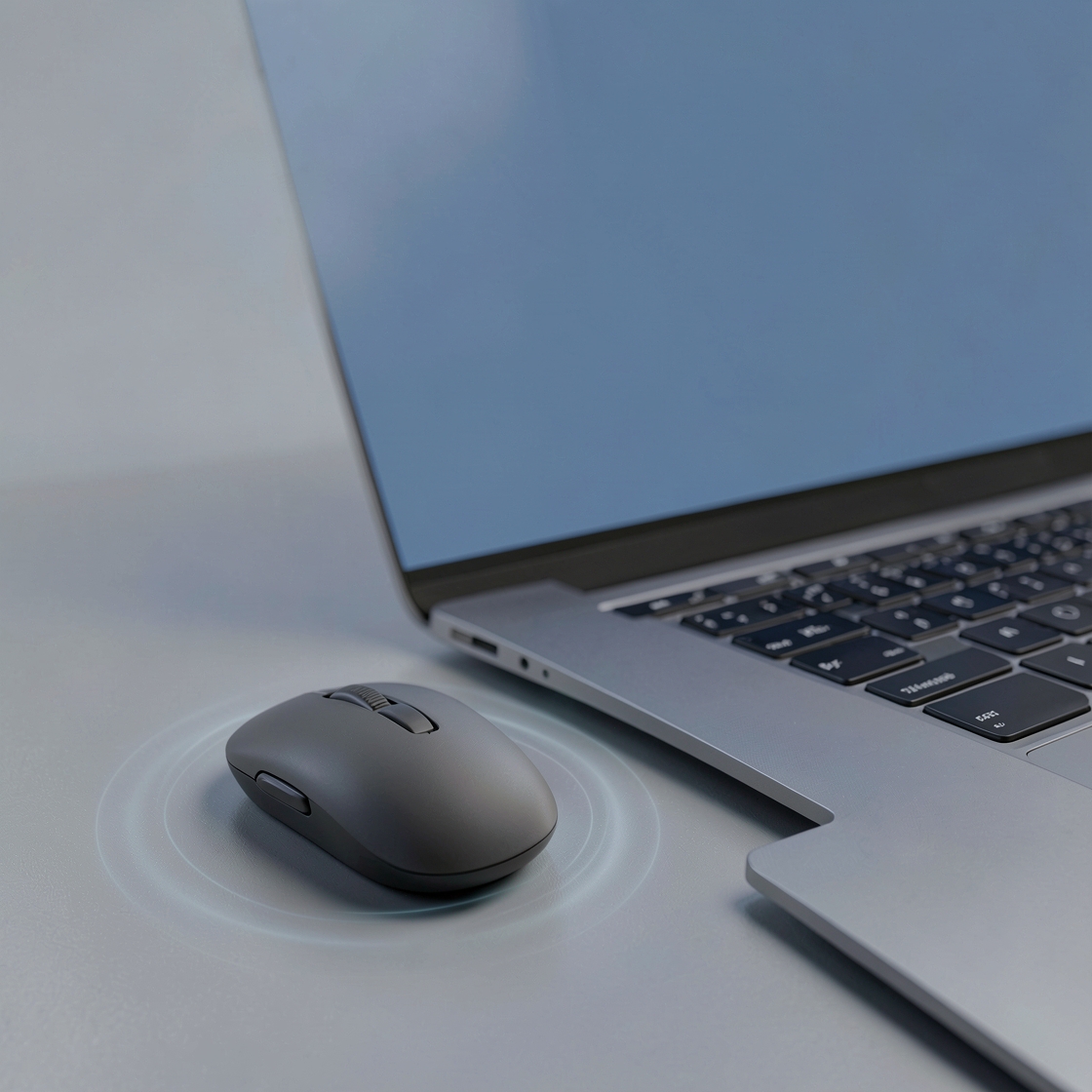 A generic dark wireless mouse beside a silver laptop on a blue-gray desk