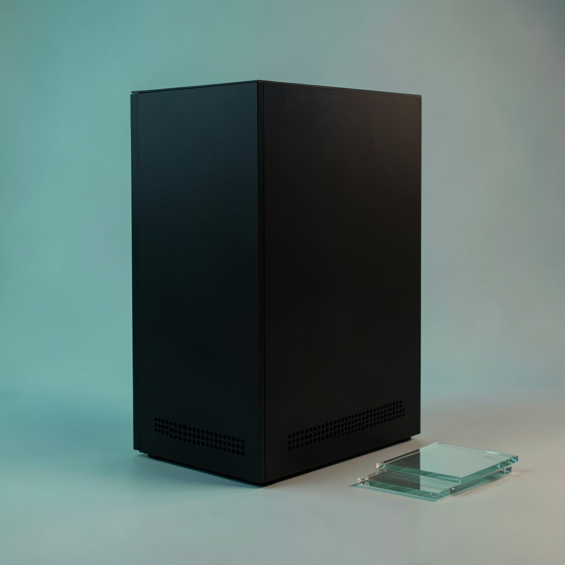 A plain black computing enclosure beside a small stack of clear glass tiles
