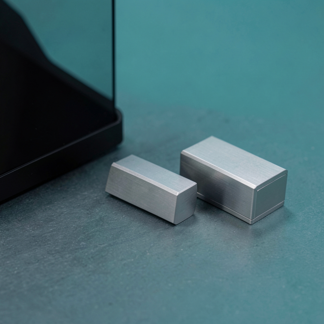 Two unmarked silver enclosures beside the corner of a dark display on a teal desk
