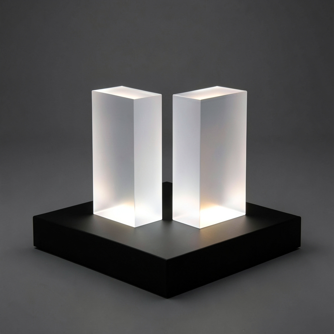 Two softly illuminated translucent columns on a square black platform against a dark background.
