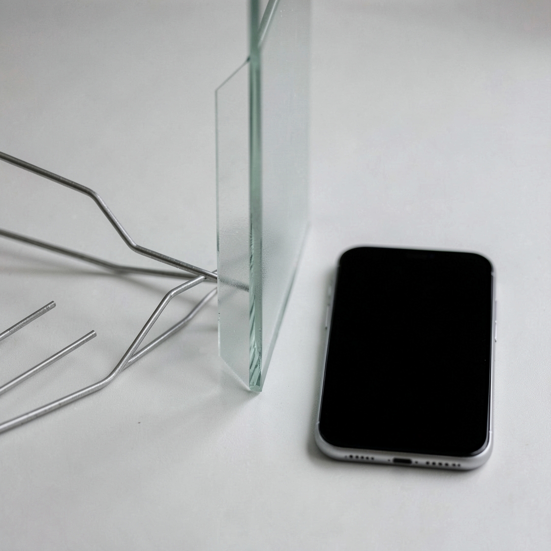 A black-screen smartphone beside a glass divider and thin metal paths
